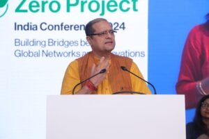 Man in an orange and brown kurta speaks at a podium during the Zero Project India Conference 2024.
